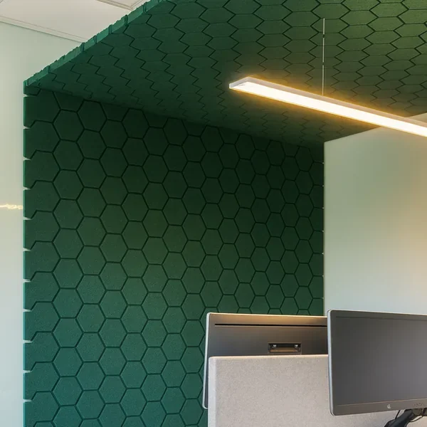 Dark green hexagon-pattern acoustic panels lining a work booth, with a linear pendant light suspended in front