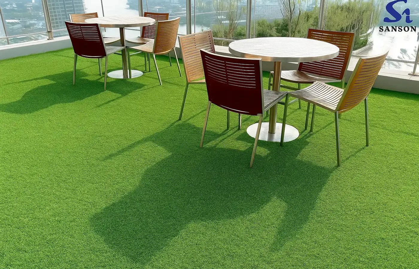 Outdoor café tables and chairs on a bright green artificial lawn in a glazed rooftop space