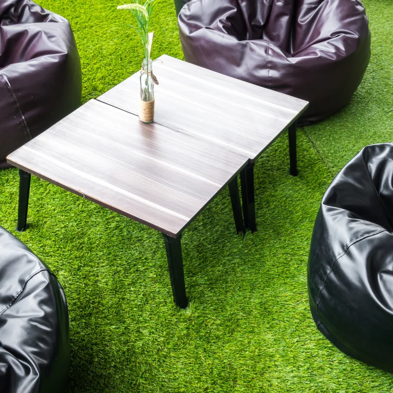 Black bean bags around a low timber table on bright green artificial grass