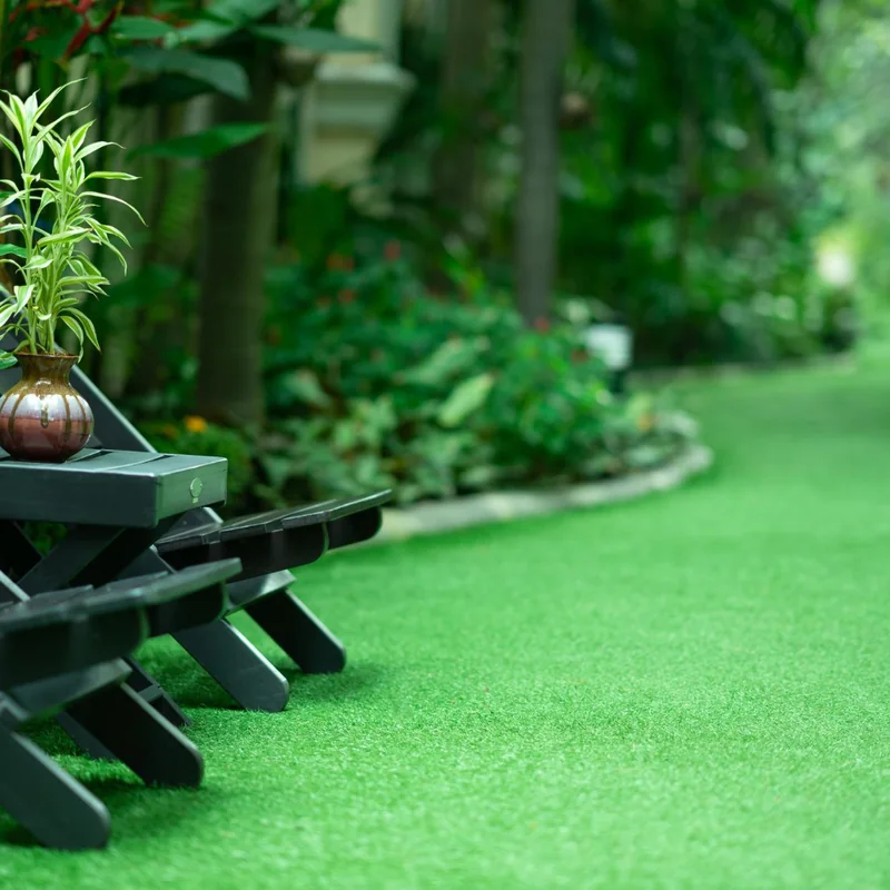 Dark green folding wooden seats with a potted plant on a green artificial lawn, with dense planting behind