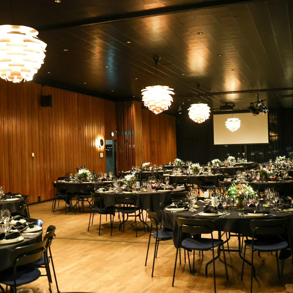 Banquet hall with timber-panelled walls, globe pendant lights and round tables set for dinner