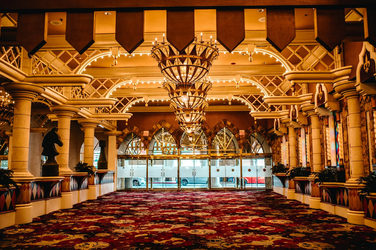 Ornate hall with gilded columns, a large crystal chandelier and a deep red carpet with a dense floral pattern