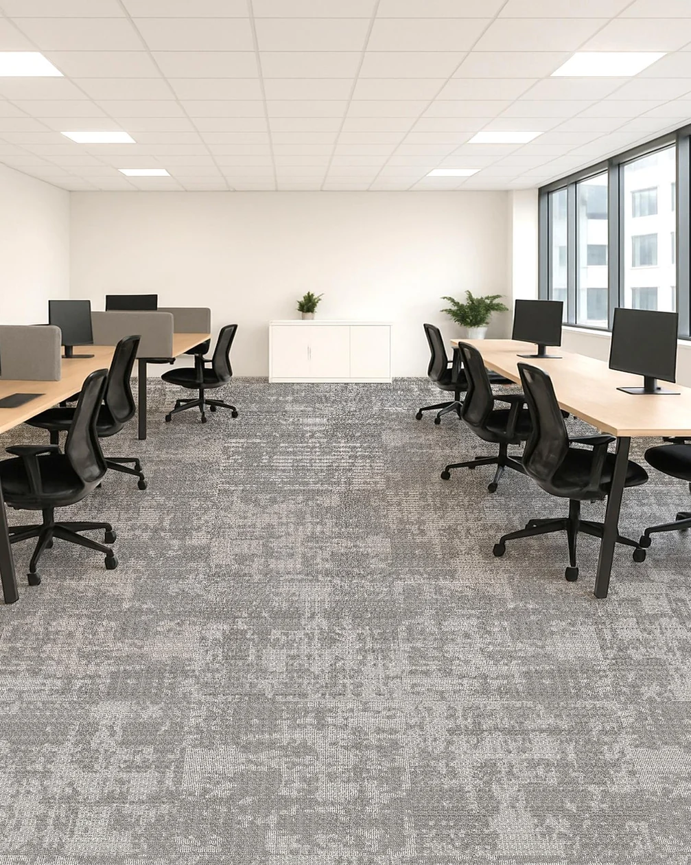 Open-plan office with two rows of timber workstations and black mesh chairs on light grey patterned carpet, beside tall windows
