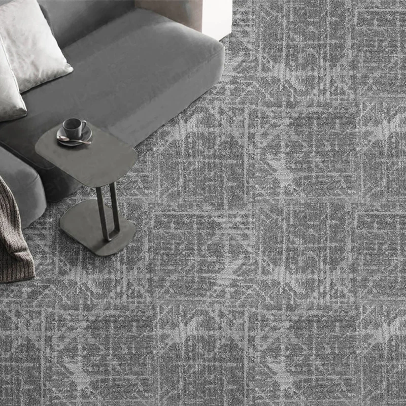 Grey sofa with cushions and a side table, seen from above, on grey carpet tiles with a fine crosshatch pattern