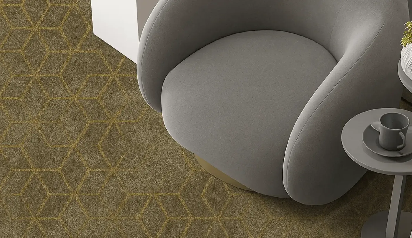 Grey curved armchair and small side table on a gold and olive broadloom carpet with a fine geometric line pattern