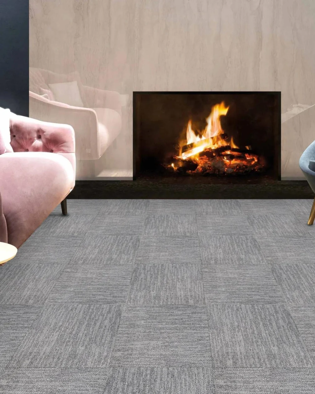 Living room with a pink velvet armchair, a navy armchair, a pouffe and a lit fireplace on light grey textured carpet tiles