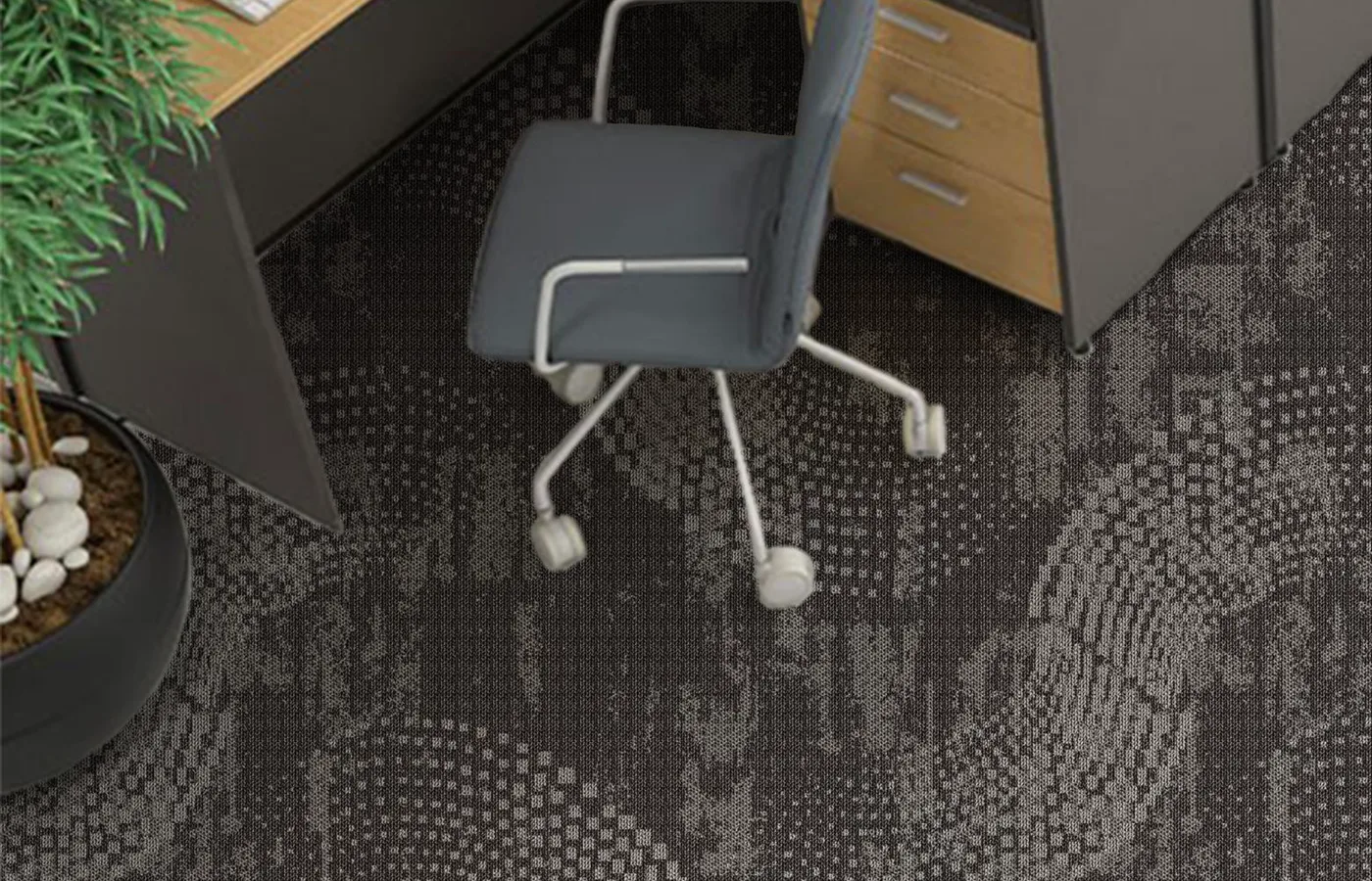 Corner workstation with a grey chair on a charcoal broadloom carpet with a dotted swirl pattern, beside a plant