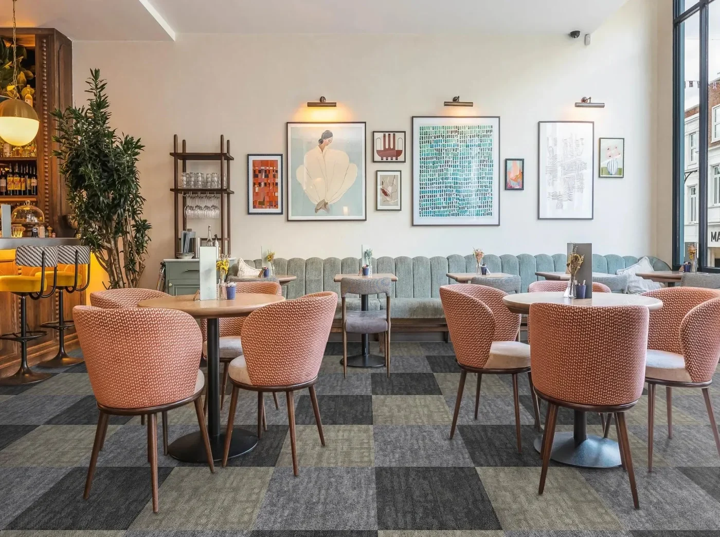 Restaurant dining area with pink upholstered chairs on a floor of square grey and olive carpet tiles laid in alternating blocks