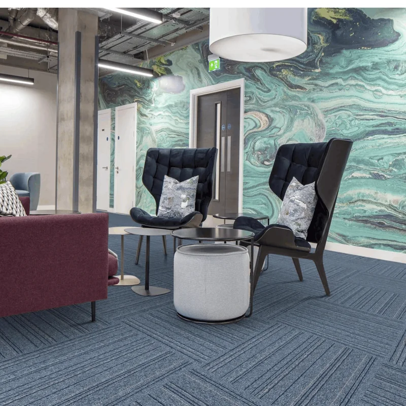 Office lounge with a burgundy sofa, black wingback armchairs and a grey pouf in front of a marbled green feature wall, on blue striped carpet tiles
