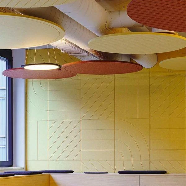 Breakout space with built-in bench seating, a yellow wall of patterned acoustic panels and round coloured acoustic clouds overhead