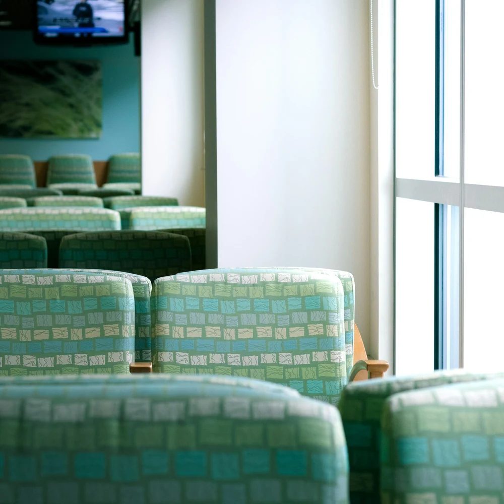 Rows of pale green upholstered waiting chairs beside a tall window