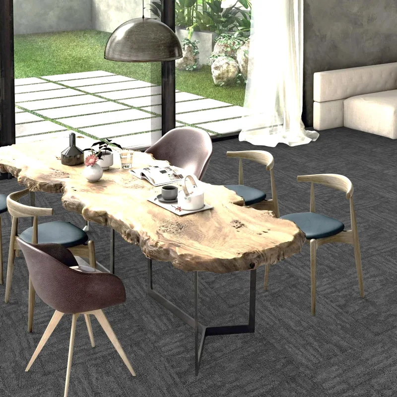 Live-edge timber dining table with grey chairs on charcoal carpet tiles beside a glass wall opening to a garden