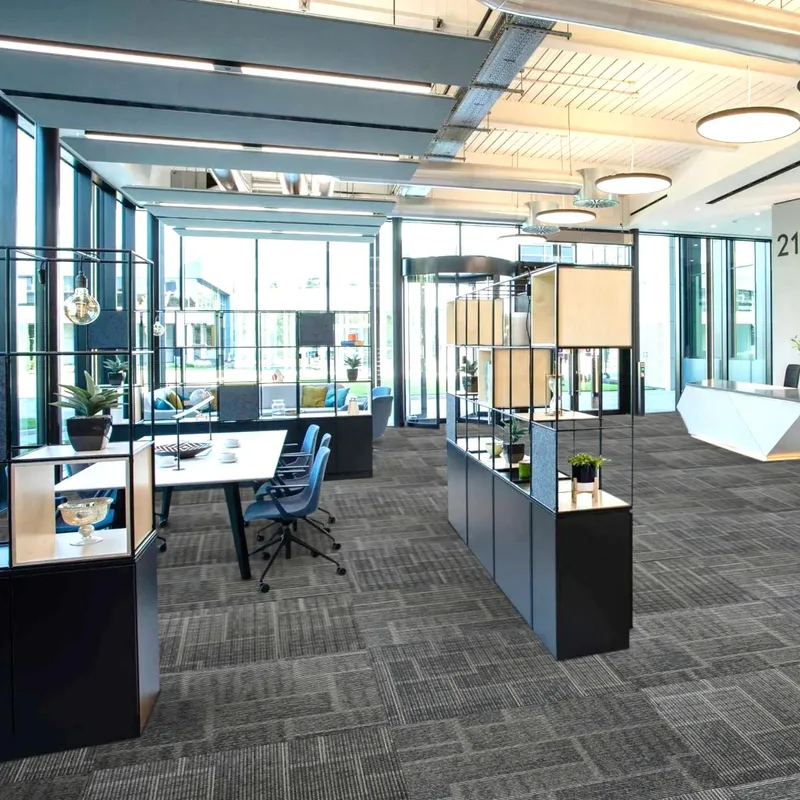 Open office with glass partitions, white desks and a reception counter on grey striped carpet tiles
