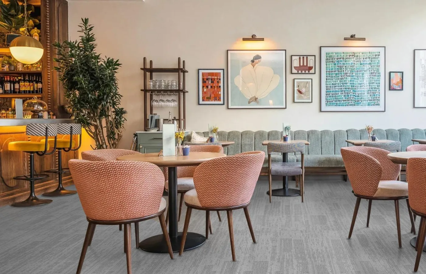 Restaurant with pink upholstered chairs, round tables and framed pictures on a light grey carpet tile floor