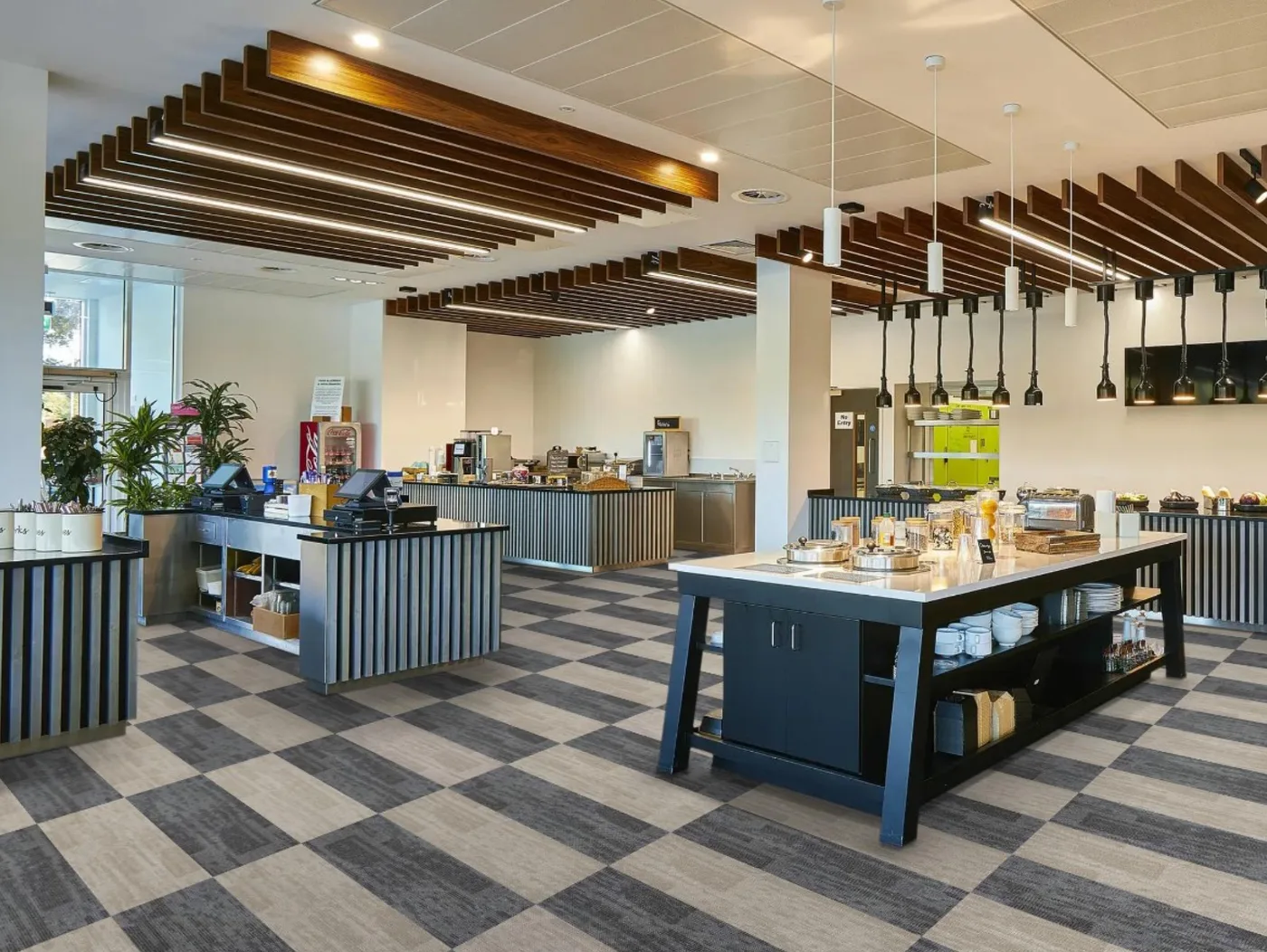 Office café and kitchen with a blue island and stools on a floor of light and dark grey carpet tiles laid in a checkerboard