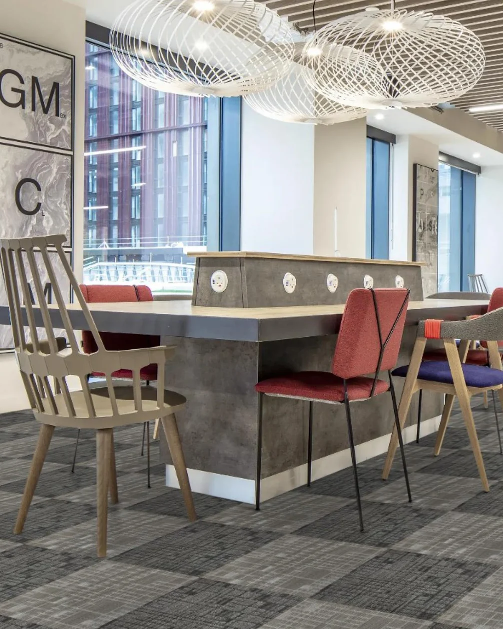 Office café with red and timber chairs around a high table on grey carpet tiles laid in a checked pattern