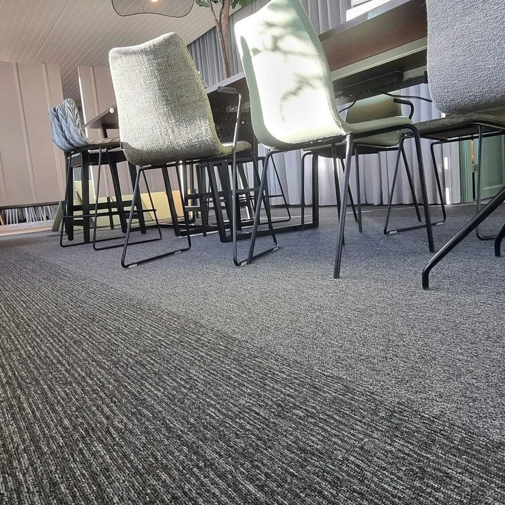 Low-angle view across a grey carpet tile floor towards office chairs and desks by a window