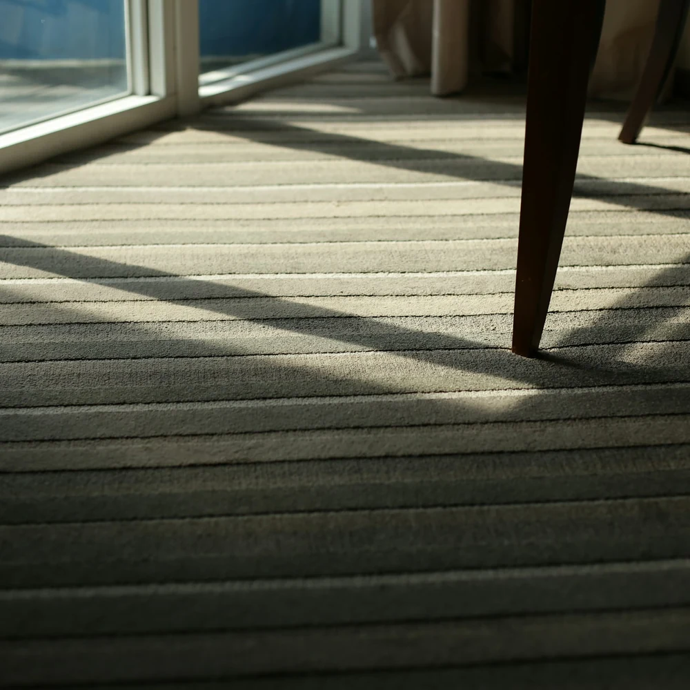 Striped carpet in warm daylight with the long shadow of a chair leg falling across it