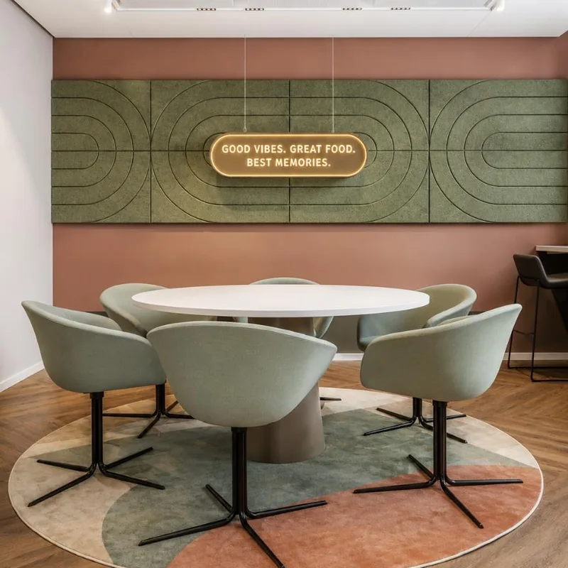 Sage green acoustic panels with curved grooves on a pink wall above a round dining table with grey tub chairs on a patterned rug