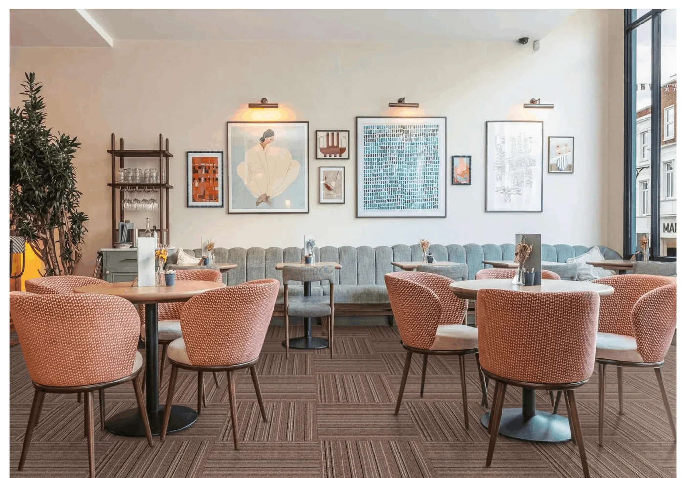 Restaurant dining room with coral patterned tub chairs, round tables and framed pictures on the walls, on brown striped carpet tiles