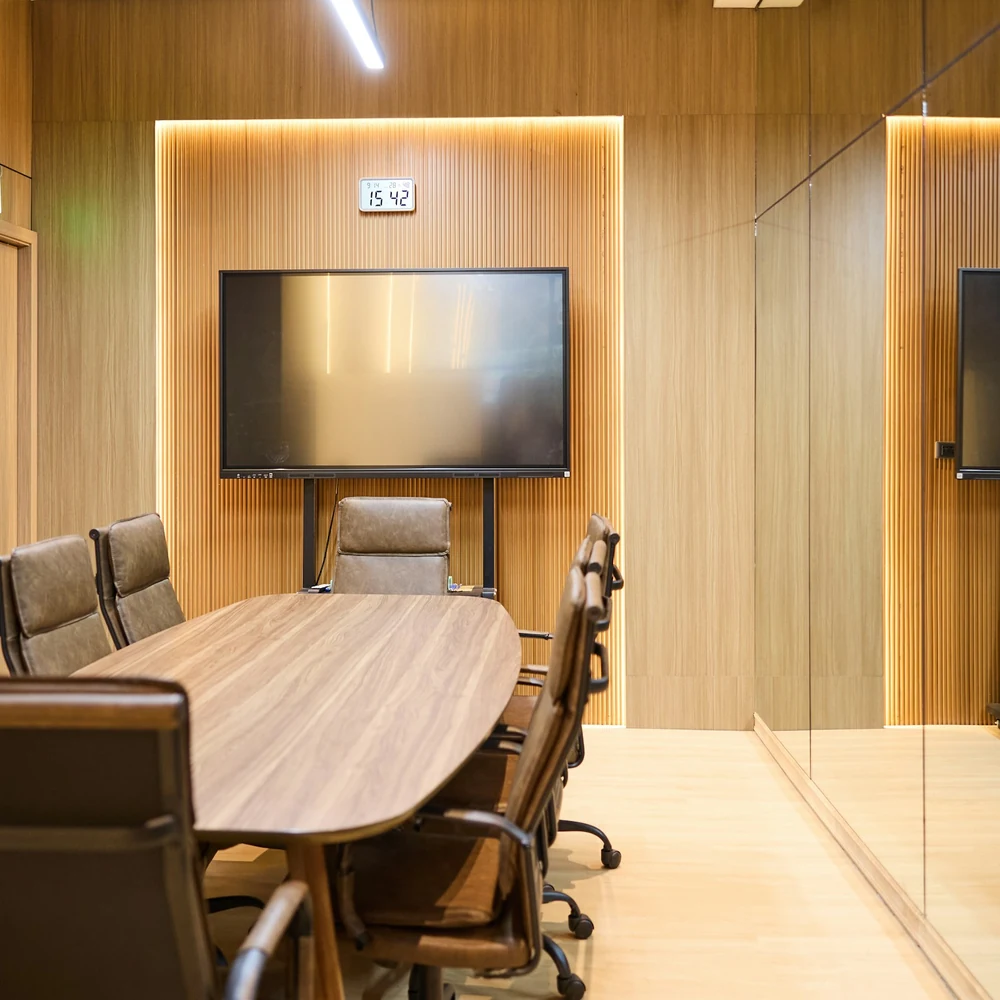Meeting room with timber-panelled walls, an oval table with leather chairs and a large wall-mounted screen