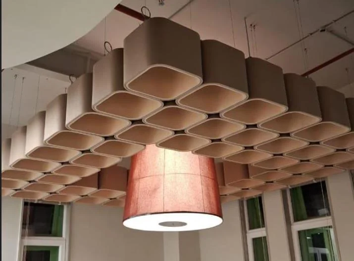Cluster of honeycomb-shaped acoustic ceiling elements in beige felt around a large salmon-pink pendant lamp
