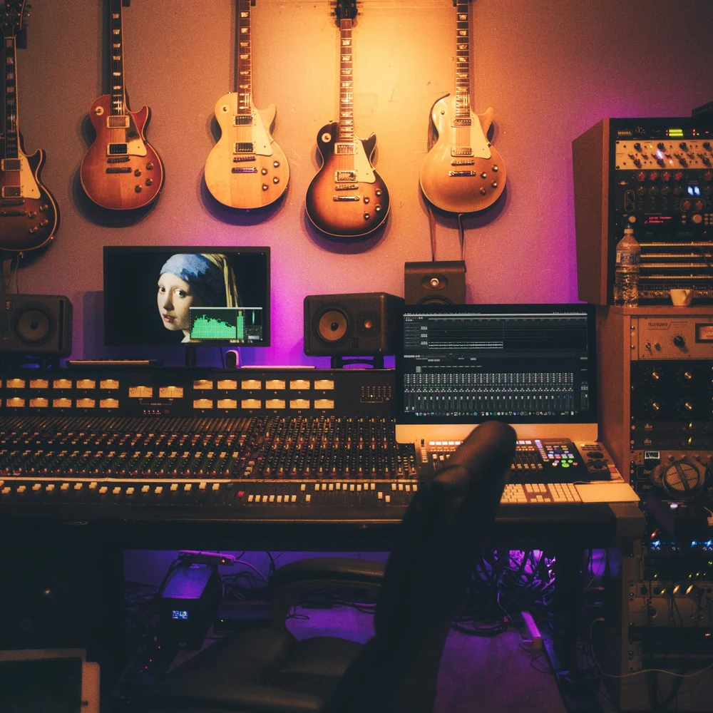 Recording studio control room with a large mixing console, studio monitors and guitars hung on a warmly lit wall