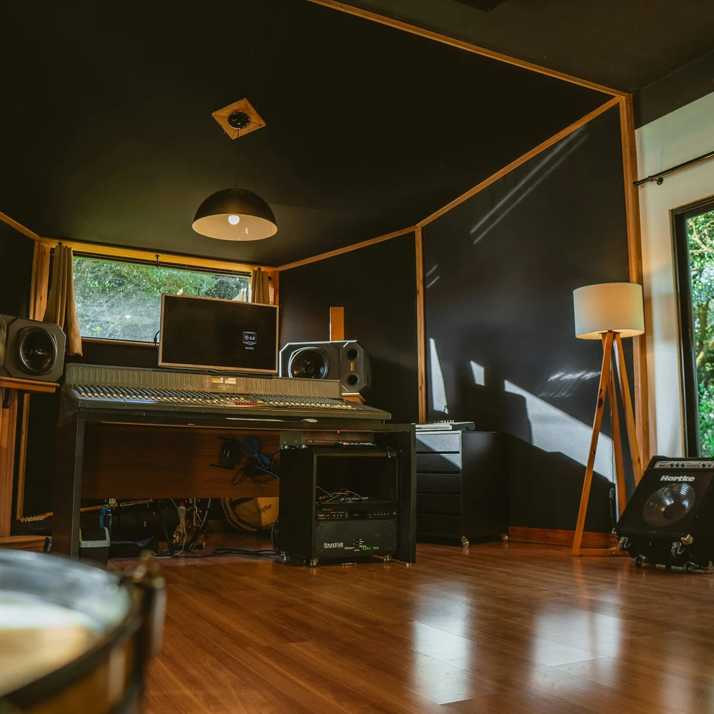 Music studio live room with dark walls, a keyboard, a guitar and tall windows onto trees