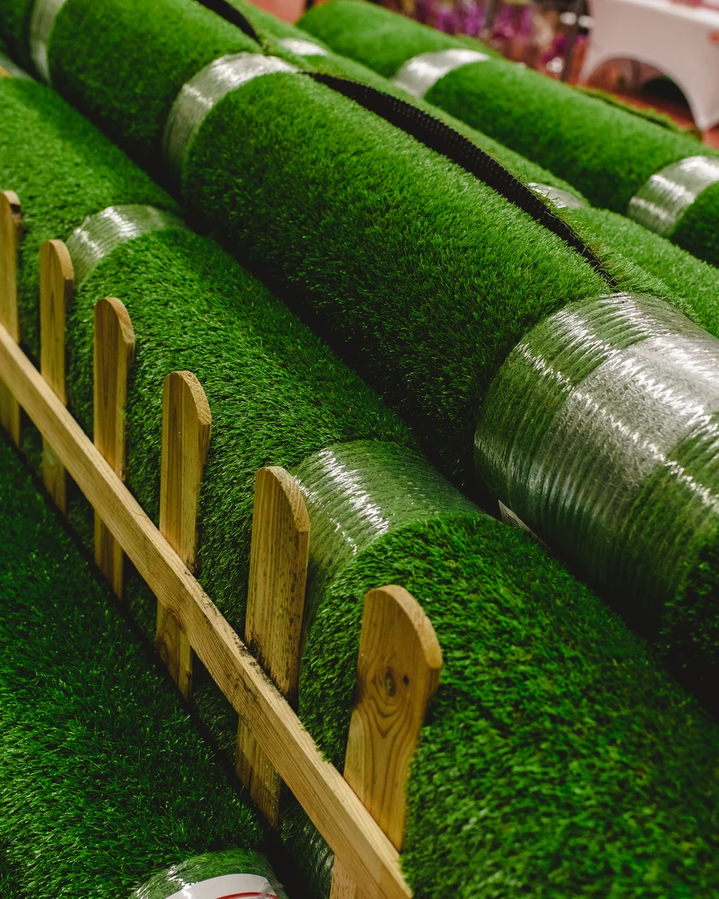 Rolls of thick green artificial grass laid in a row beside a low timber fence