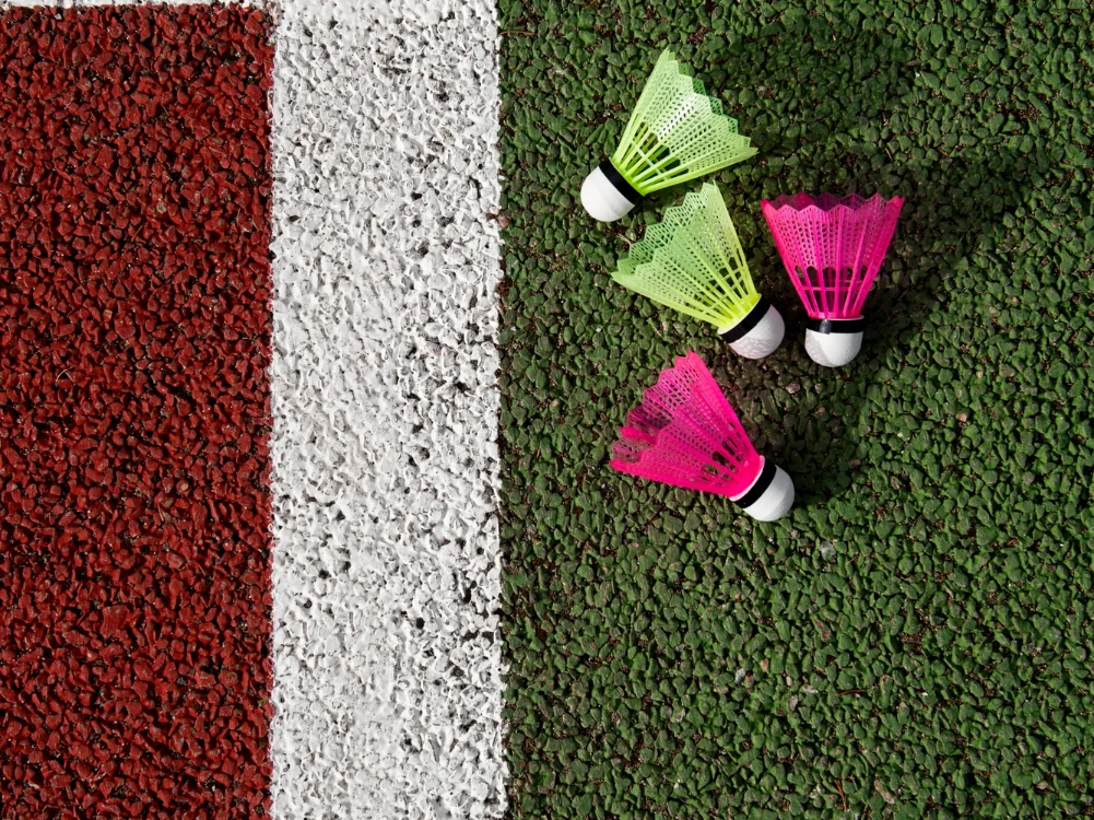 Three shuttlecocks beside a white boundary line on a green artificial turf court with a red margin