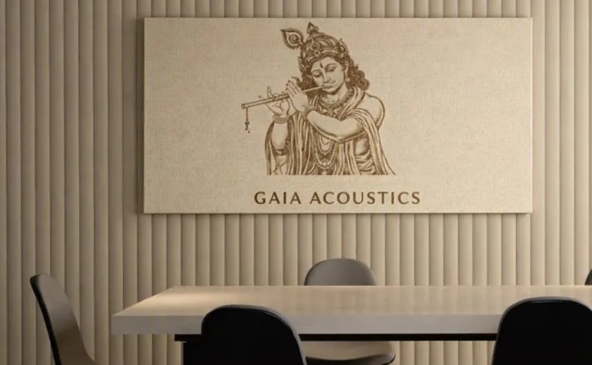 Meeting room with a vertically grooved sand-coloured acoustic wall and a carved panel showing Krishna playing the flute above the words GAIA ACOUSTICS