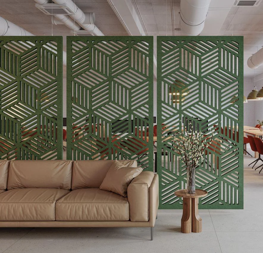 Tall green acoustic screen with a geometric cut-out pattern behind a tan leather sofa and a small plant